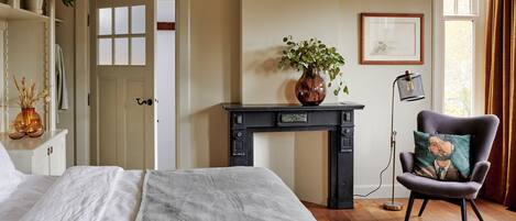 A bedroom with a bed, a dresser, a desk with a vase, a chair, and a window with curtains.