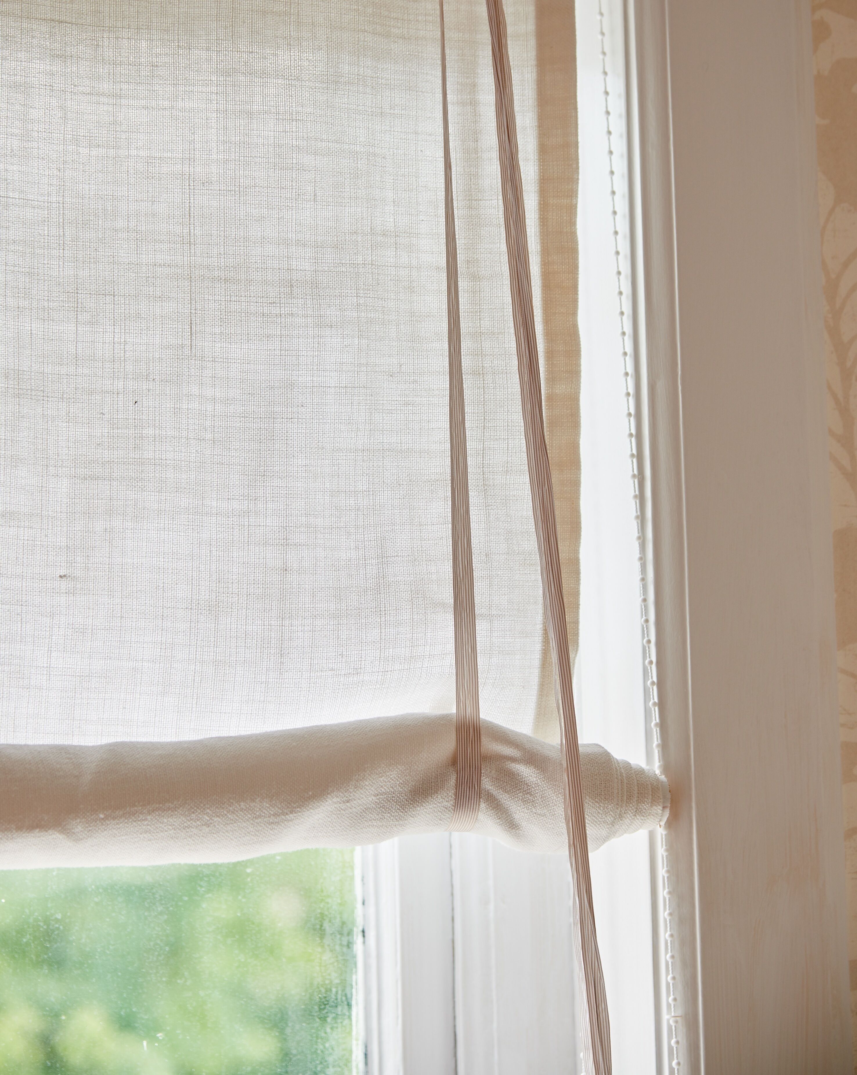 A window with a sheer white curtain and a white blind partially drawn.