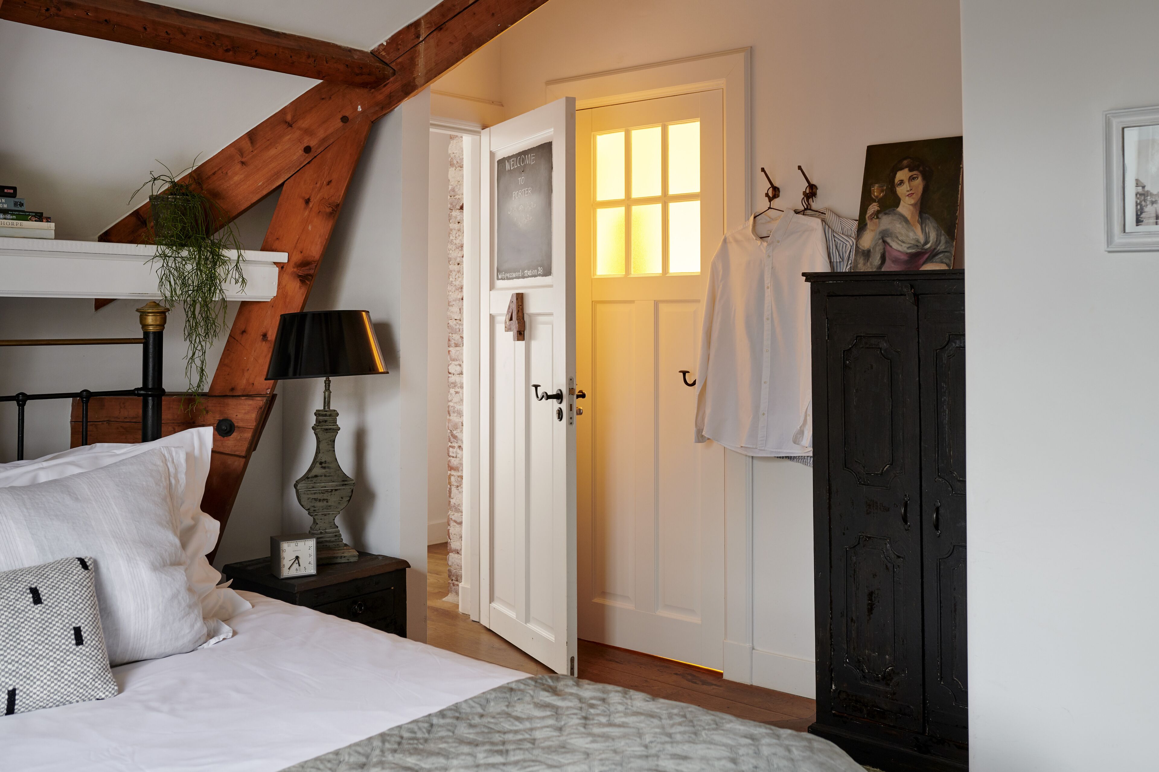 A bedroom with a bed, a nightstand, a lamp, a dresser, and a door leading to another room.
