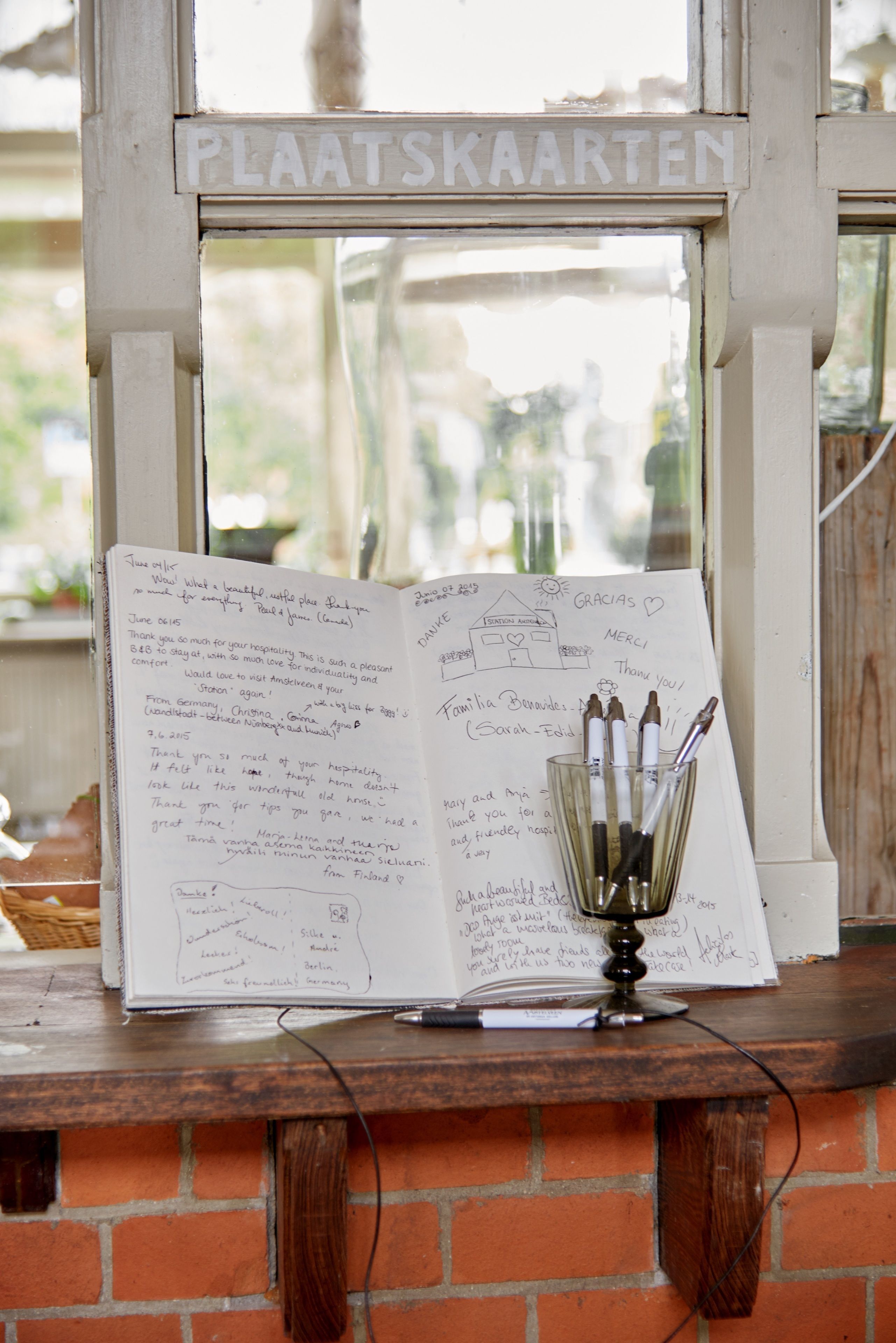 A window with the sign "PLAATSKAARTEN" and a notebook with handwritten notes on a wooden table.