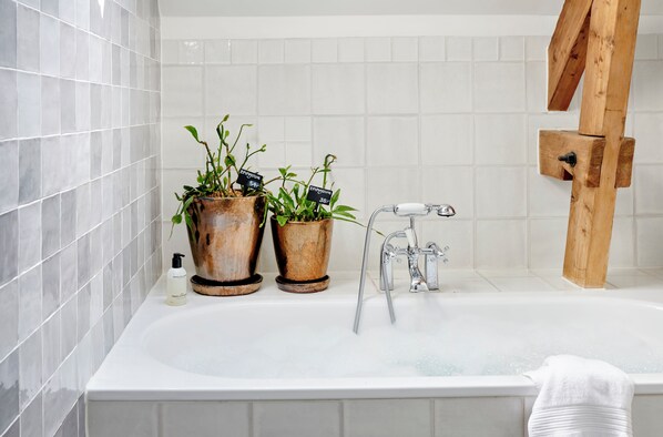 A bathroom with a white bathtub, two potted plants, a bottle of shampoo, and a wooden towel rack.
