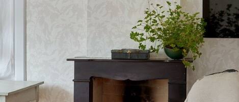 Una habitación con chimenea, un sillón con cojín amarillo y una planta en maceta.