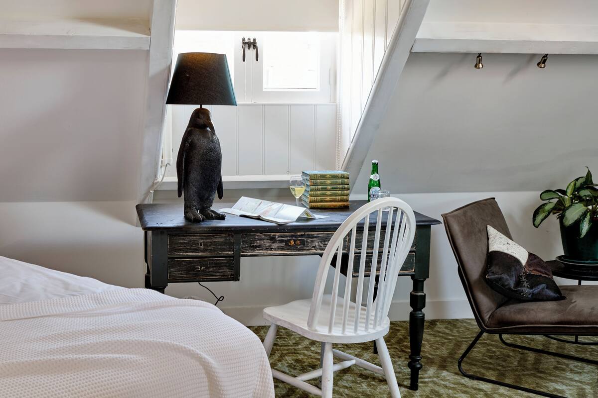 A study with a desk, a chair, a lamp, books, a bottle, and a plant.