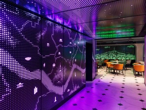 A modern interior with a digital LED wall displaying various icons, a seating area with tables and chairs, and a patterned floor. - ibis Styles Ambassador Seoul Myeongdong (Seoul)