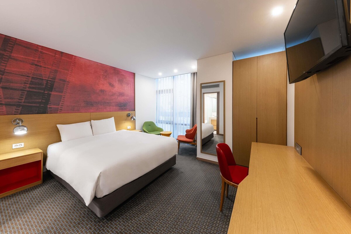 Una habitación de hotel con una cama grande, un escritorio, un televisor y un espejo.