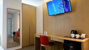Une chambre d’hôtel avec un bureau en bois, une chaise rouge, un téléviseur fixé au mur et une machine à café posée sur le bureau.