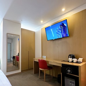 Une chambre d’hôtel avec un bureau en bois, une chaise rouge, un téléviseur fixé au mur et une machine à café posée sur le bureau.
