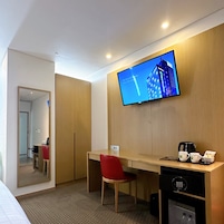 A hotel room with a wooden desk, a red chair, a television mounted on the wall, and a coffee maker on the desk.