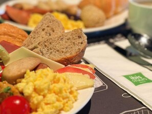 Ein Frühstücksteller mit Rührei, Käse, Brot und Tomaten.