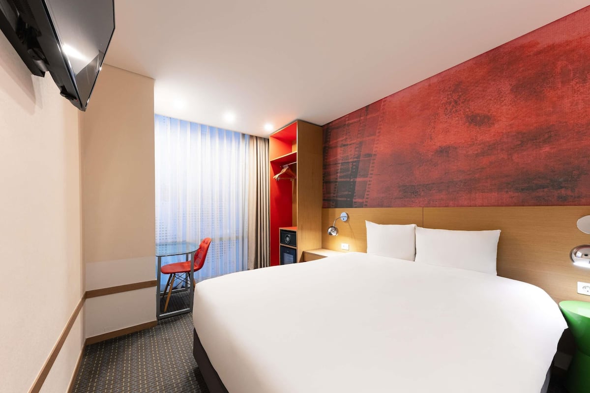 Hotellihuone, jossa on suuri sänky, työpöytä, tuoli ja televisio.