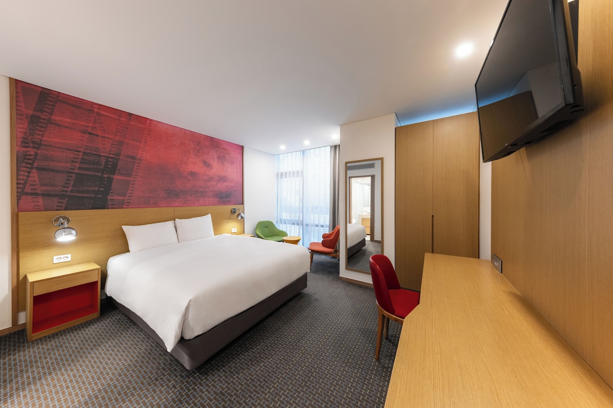Une chambre d’hôtel comprenant un lit, une table de chevet, une télévision et un bureau avec une chaise.
