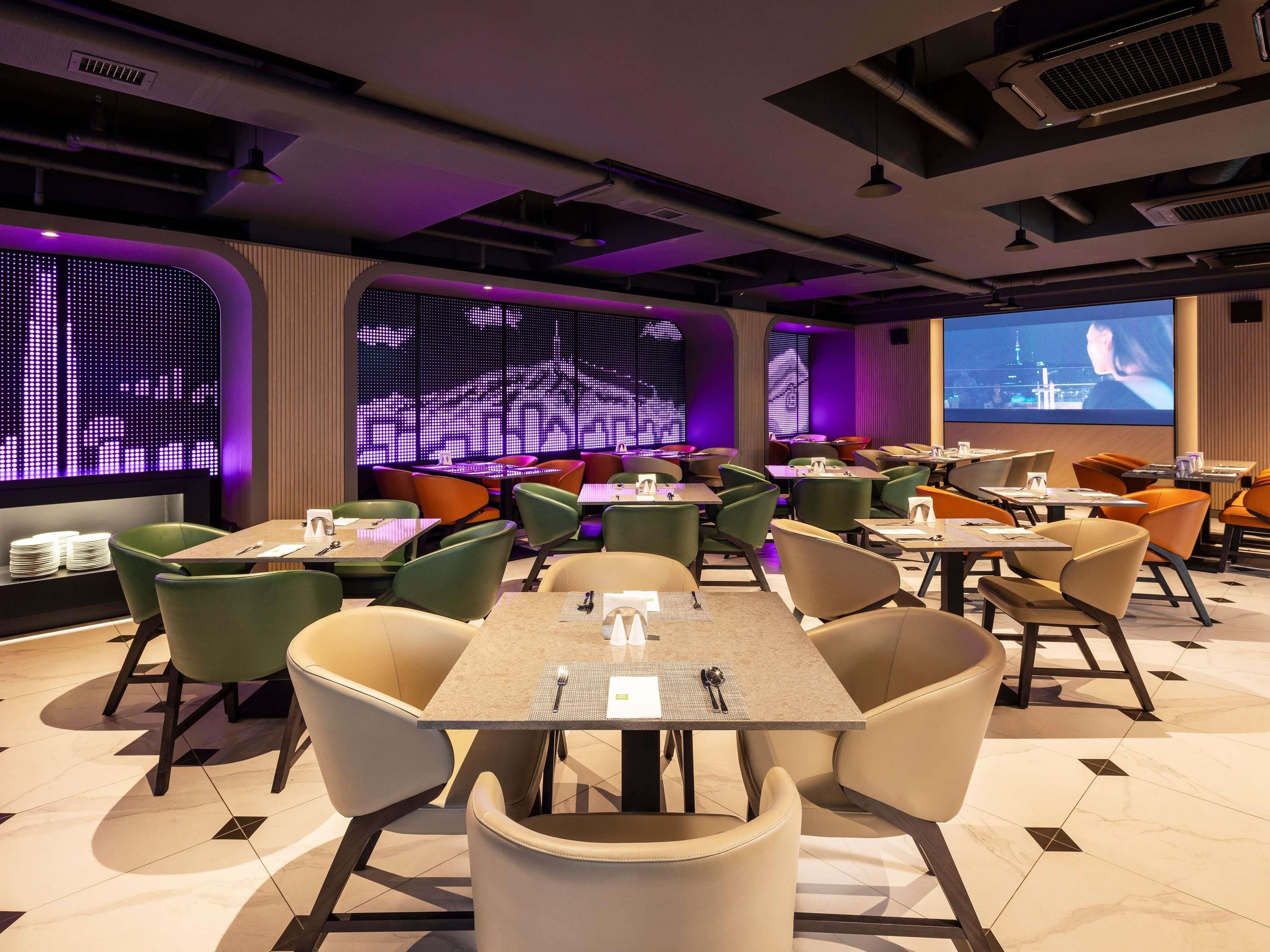 A modern restaurant with a variety of seating options, including booths and tables, and a large digital screen displaying a cityscape.