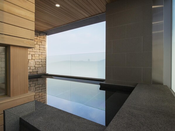 Un baño moderno con cabina de ducha de vidrio, pared de piedra y techo de madera.