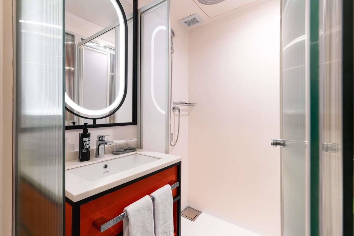 Un baño moderno con cabina de ducha de vidrio, un espejo redondo y un tocador con toallero.