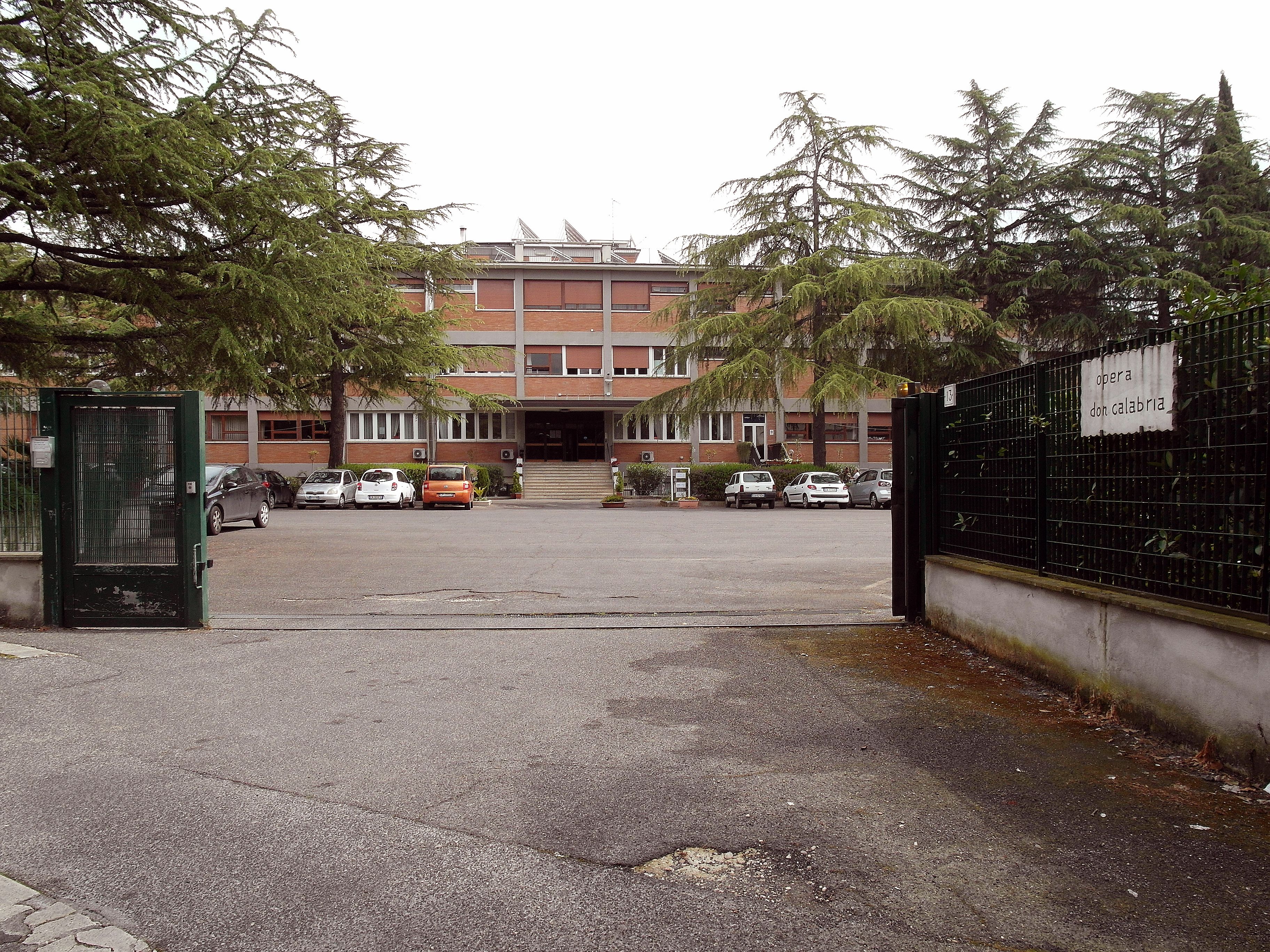 A parking lot with several cars, a building with a brick facade, and a sign that reads "opera don galabria".