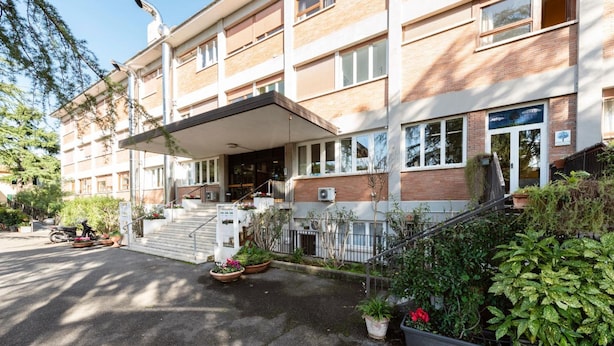 A multi-story building with a covered entrance, outdoor seating area, and potted plants. - Opera Don Calabria Casa per Ferie (Rome)