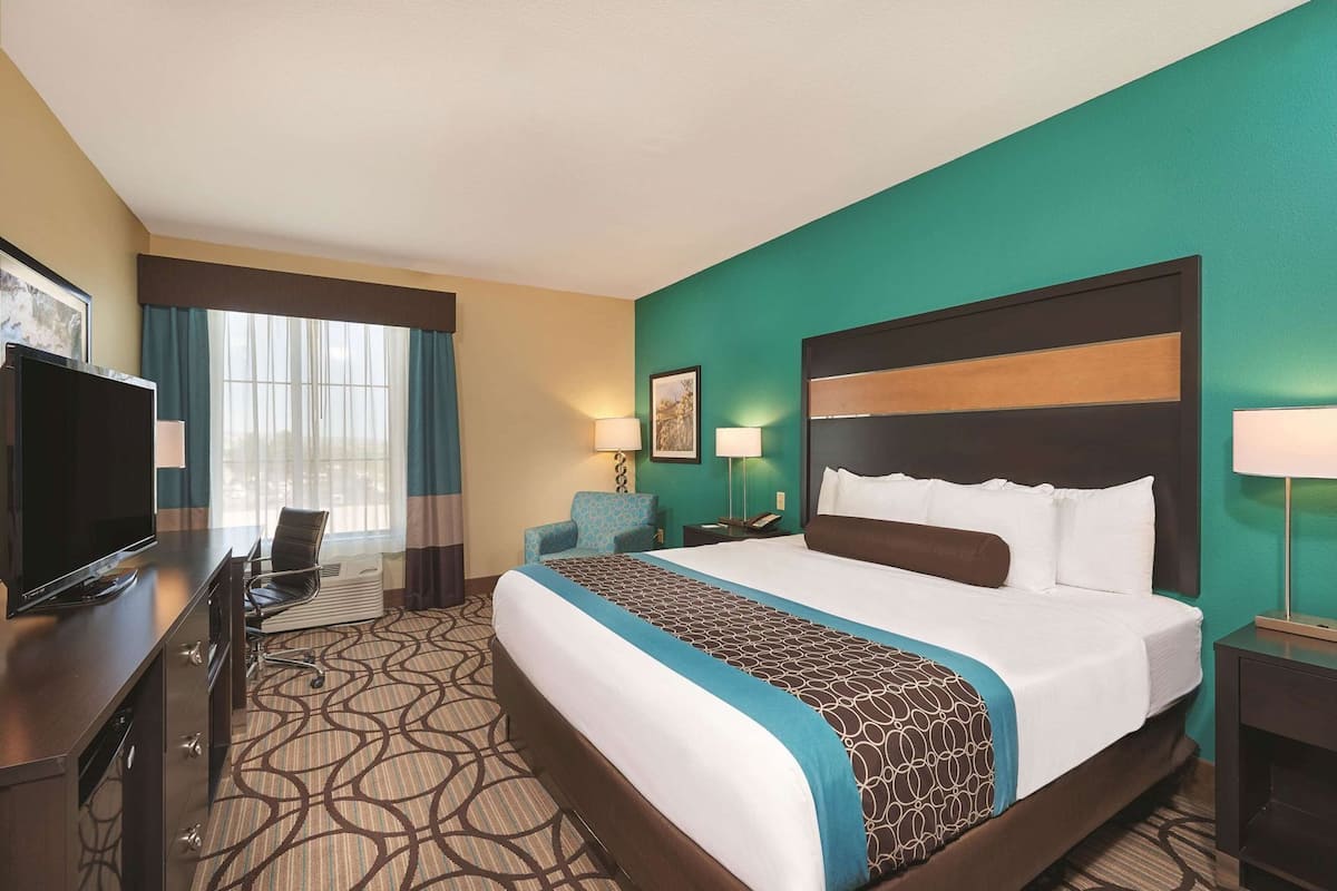 A hotel room with a large bed, a television, a desk with a chair, and a window with curtains.