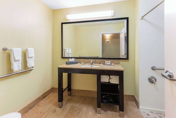 A bathroom with a sink, mirror, towel rack, and a shower area.