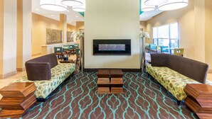 A lobby with a patterned carpet, sofas, a flat-screen TV, and pendant lighting. - La Quinta Inn & Suites by Wyndham Carlsbad (Carlsbad)