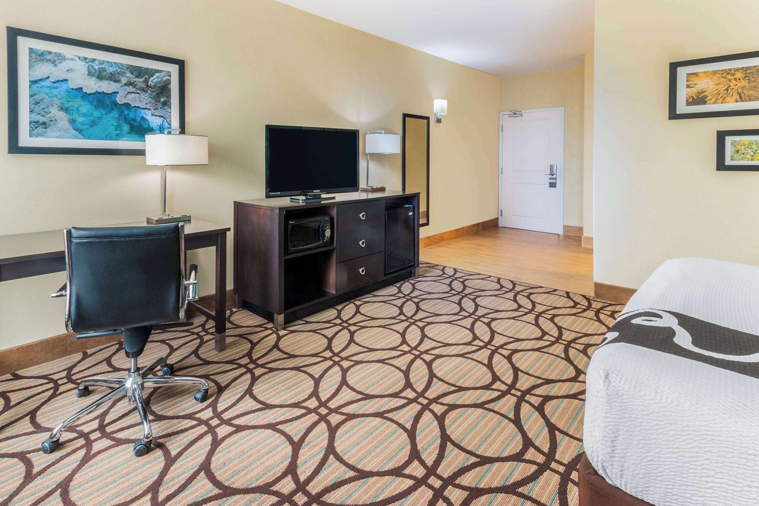 A hotel room with a bed, a desk with a computer, a television, a microwave, and a door.