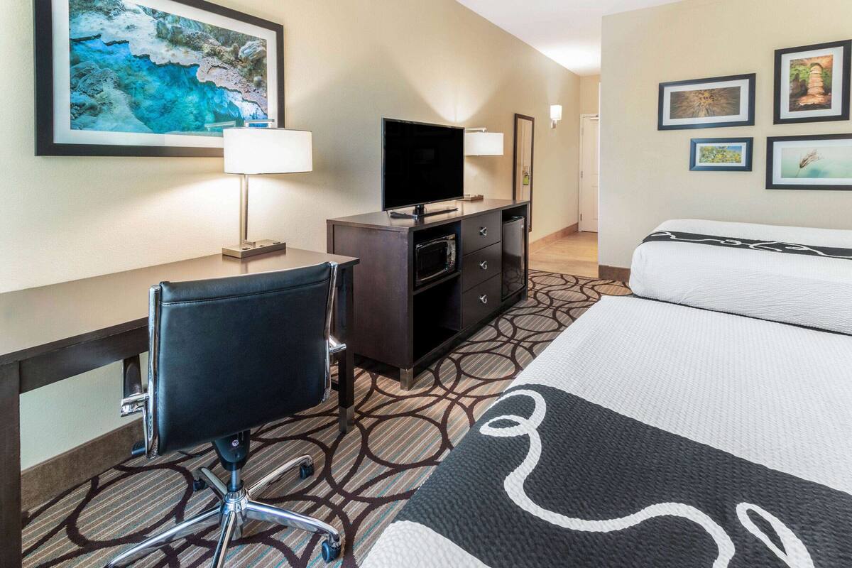 A hotel room with a bed, a desk with a chair, a television, a microwave, and a dresser.