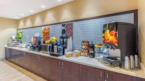 A buffet counter with various food and drink options, including a coffee station with multiple coffee makers and a fruit juice dispenser. - La Quinta Inn & Suites by Wyndham Carlsbad (Carlsbad)