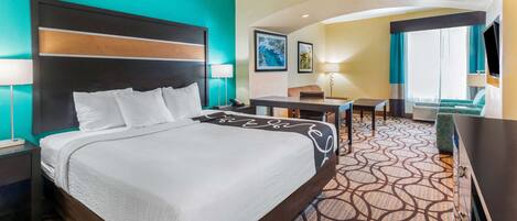 A hotel room with a large bed, a desk, a chair, and a TV.
