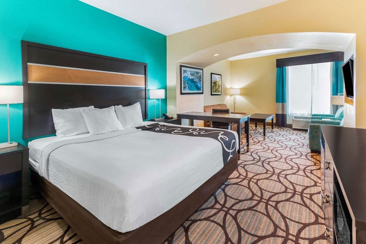 A hotel room with a large bed, a desk, a chair, a TV, and a window with curtains.
