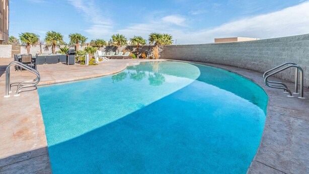 A curved swimming pool with clear blue water, surrounded by a concrete deck and palm trees. - La Quinta Inn & Suites by Wyndham Carlsbad (Carlsbad)