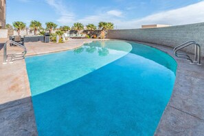 Une piscine aux bords incurvés, avec une eau d’un bleu cristallin, entourée d’une terrasse en béton et de palmiers.
