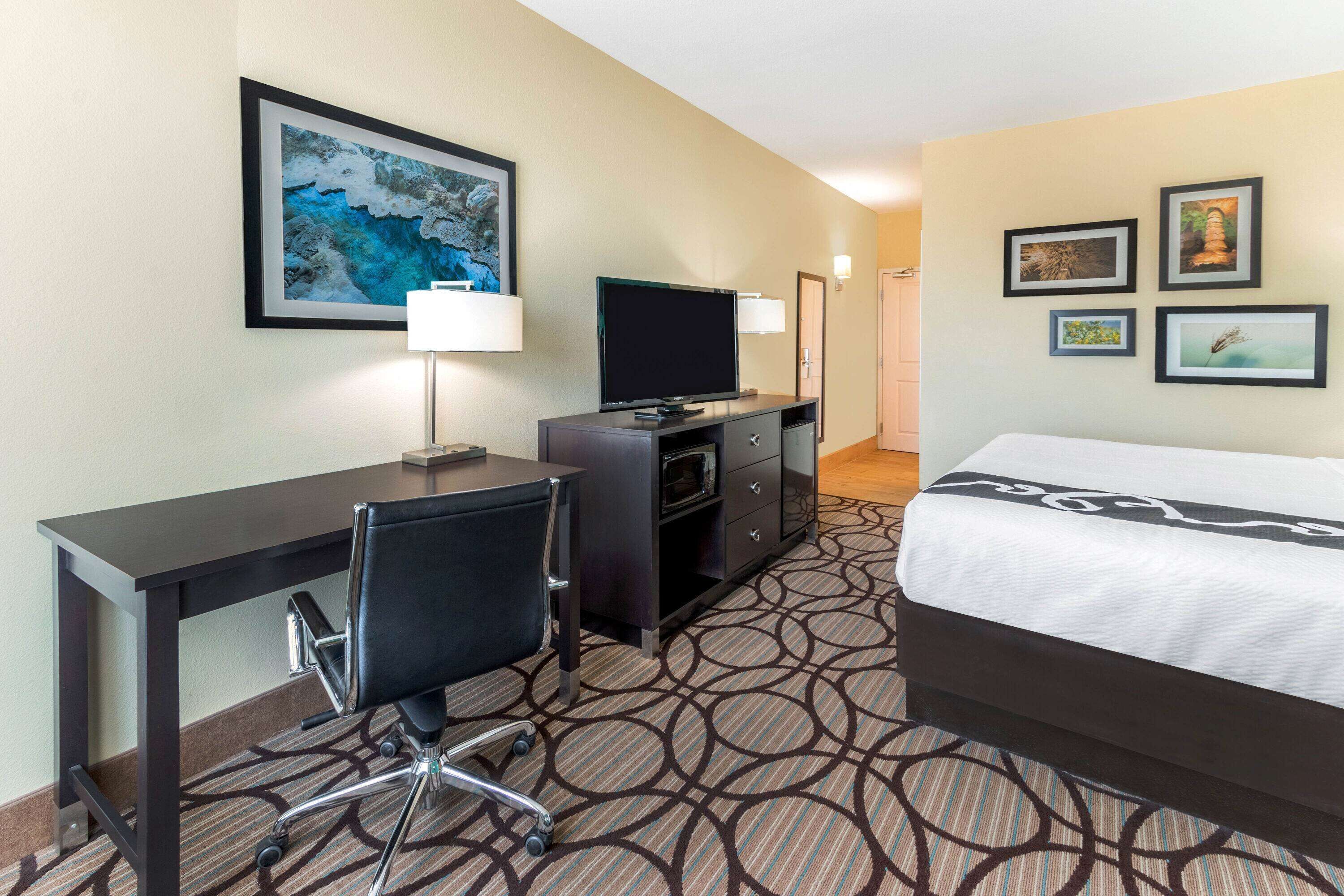 A hotel room with a bed, desk, chair, TV, and wall art.