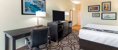 A hotel room with a bed, desk, chair, TV, and wall art.
