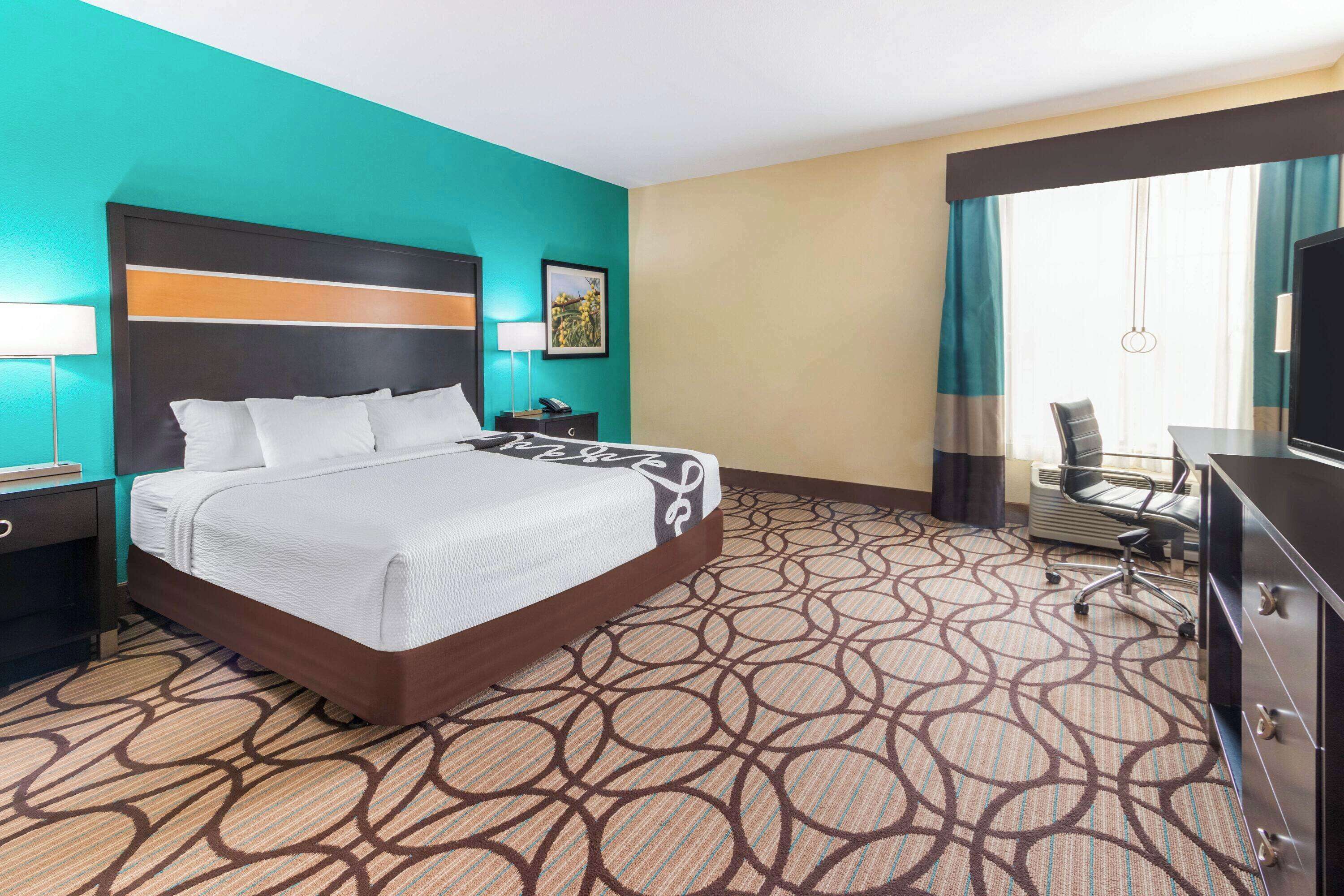 A hotel room with a large bed, a desk with a chair, a TV, and a window with curtains.
