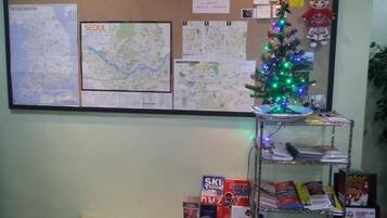 A bulletin board with maps and a Christmas tree, a small table, and a shelf with travel brochures.