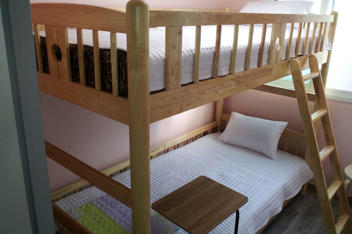 Una cama tipo litera con escalera de madera, una mesita de madera y una ventana con luz natural.
