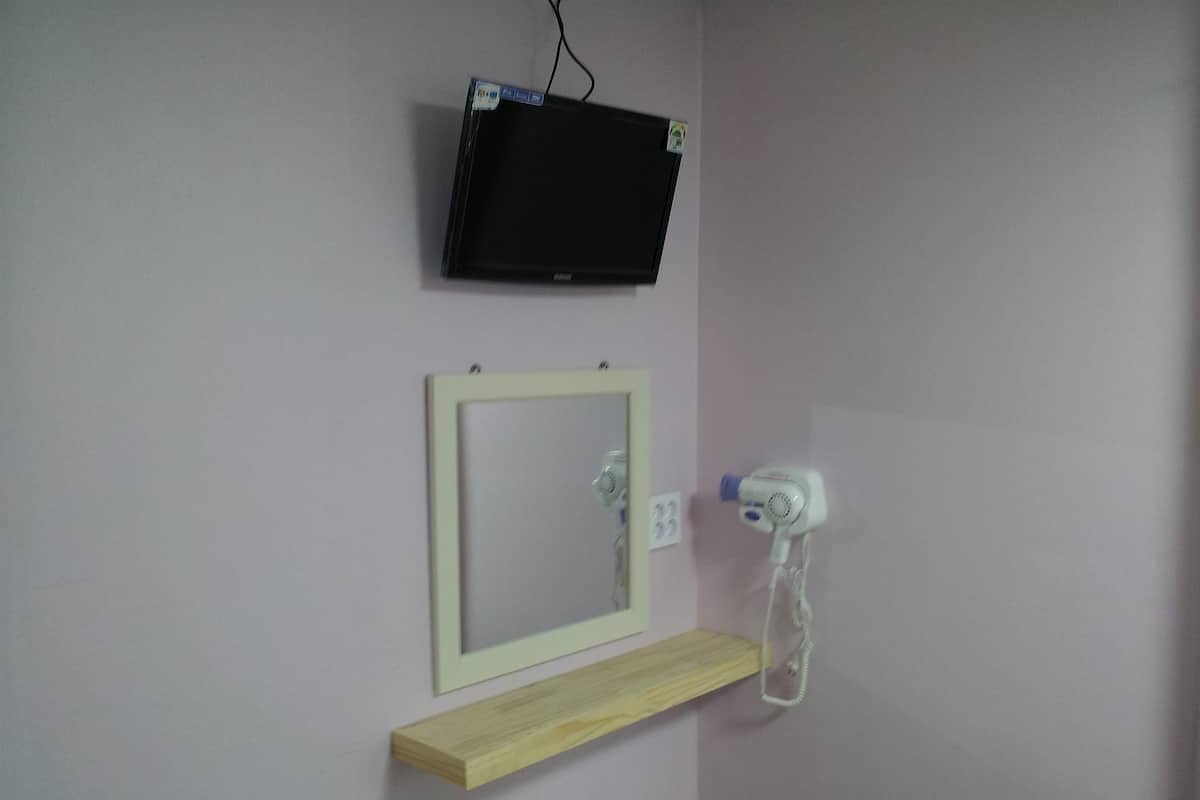 Un baño con televisión montada, espejo, repisa y secador de pelo.