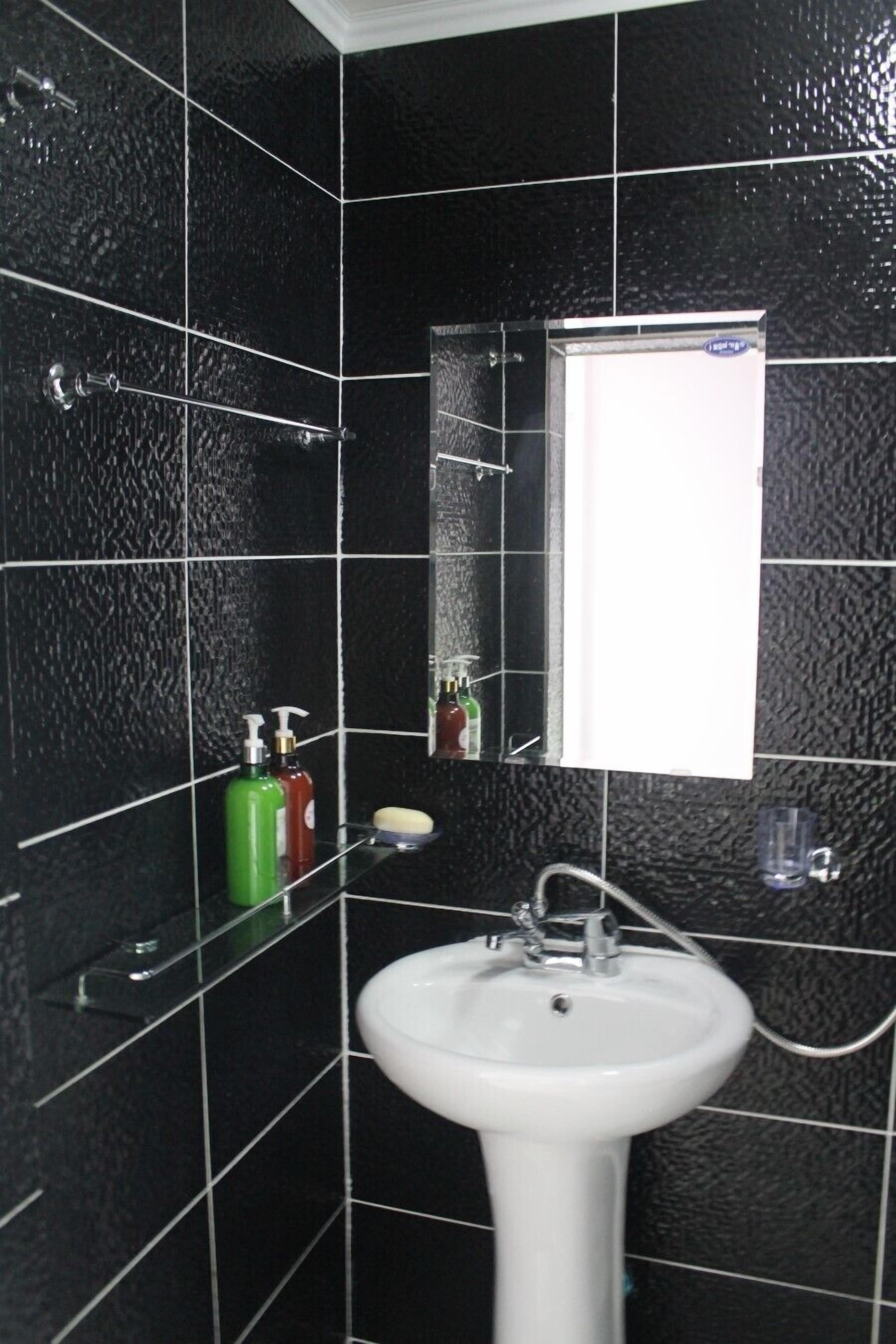 A bathroom with black tiled walls, a white sink, and a mirror.