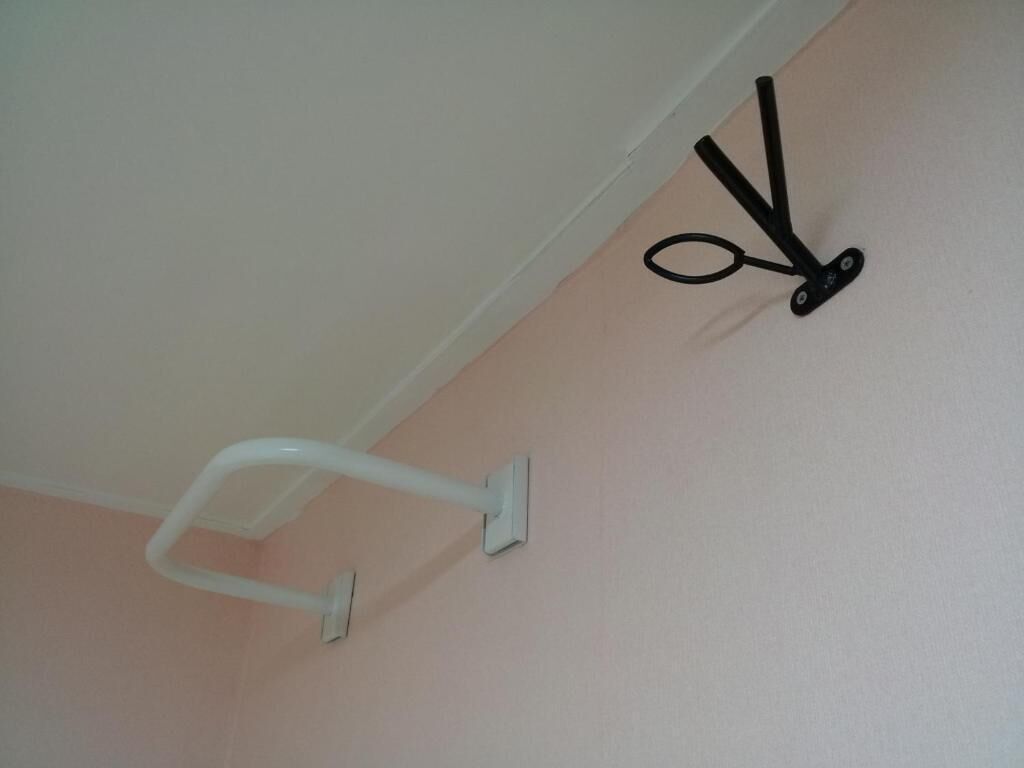 Eine weiße Haltestange an der Decke und ein schwarzer Haken an der Wand.