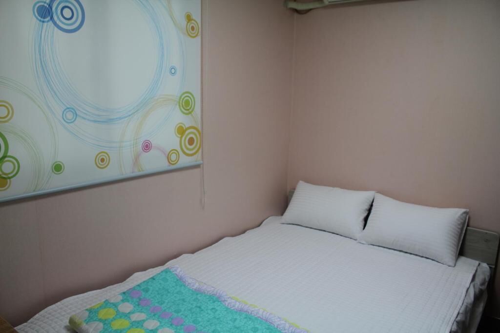 Un dormitorio con una cama, un almohadón blanco y un cuadro abstracto colorido en la pared.