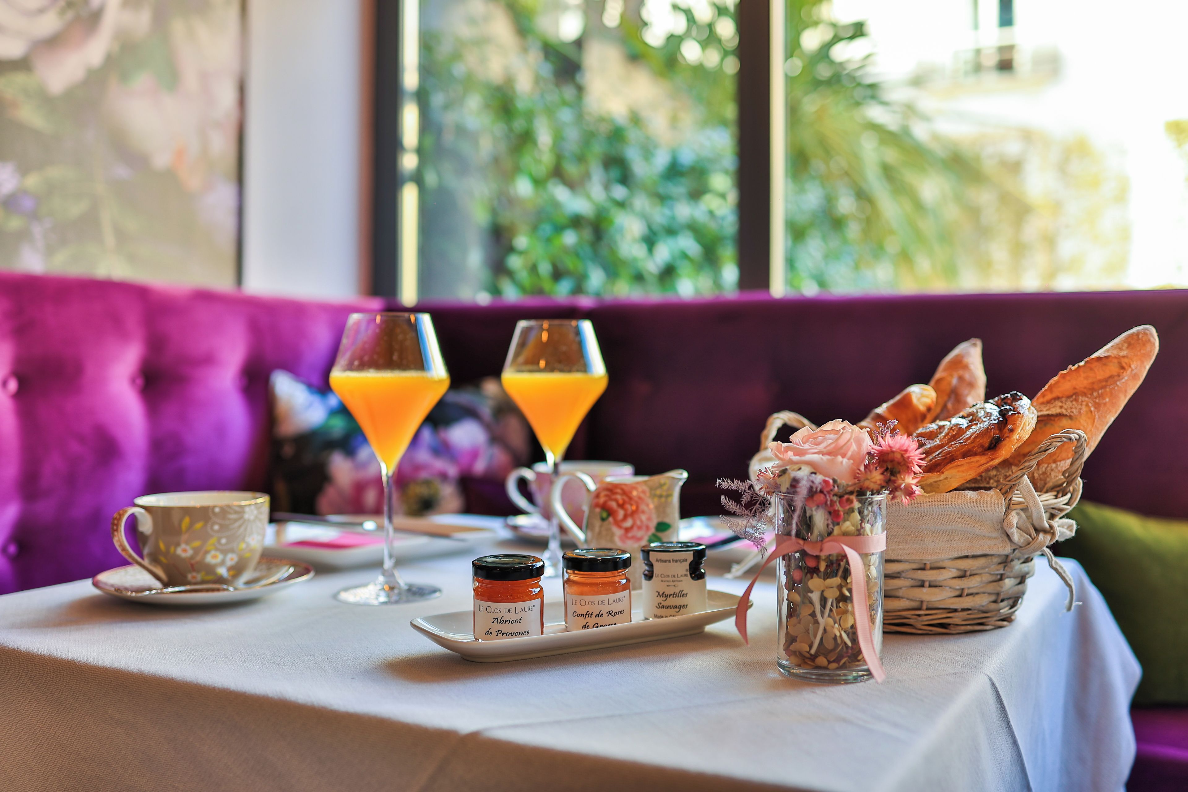 Mesa posta com copo de suco de laranja, xícara, cesta de pão e potes de condimentos.
