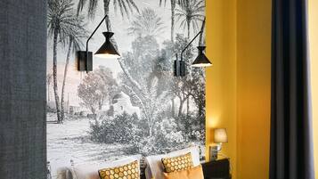 Camera d'albergo con un letto grande, due comodini, un murale con palme e una tenda scura.