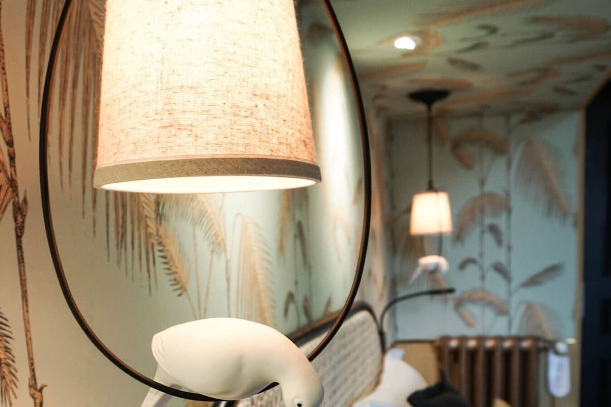 A bed with a white headboard, a round mirror, and a lamp.