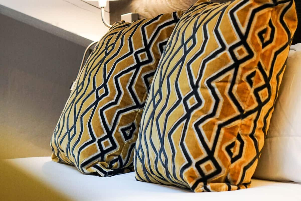 A corner of a room with a white wall, a dark wooden headboard, and two patterned pillows on a white sofa.