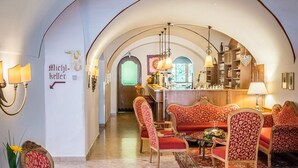 Eine großzügige Lobby mit hoher, gewölbter Decke, roten, gepolsterten Sesseln, einem gemusterten Teppich und einer Bar mit hängenden Lampen.