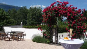 Eine Terrasse mit einem runden Esstisch, umgeben von Stühlen, mit roten Blumen und Grün im Hintergrund.