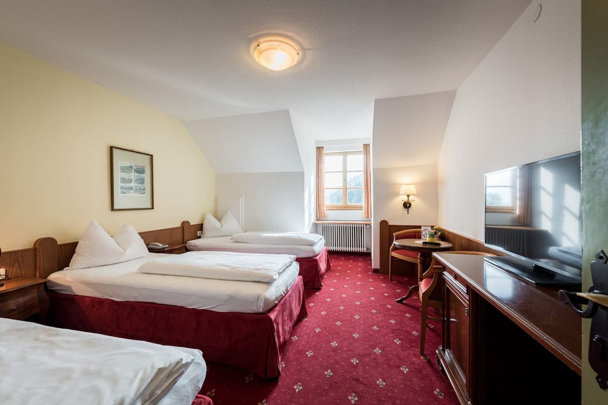Une chambre d’hôtel avec deux lits, un bureau, une télévision et une fenêtre avec des rideaux.