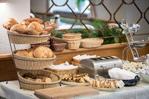 A buffet table with various breads and pastries, a toaster, and a coffee machine. - Hotel Plankenhof B&B (Pill)