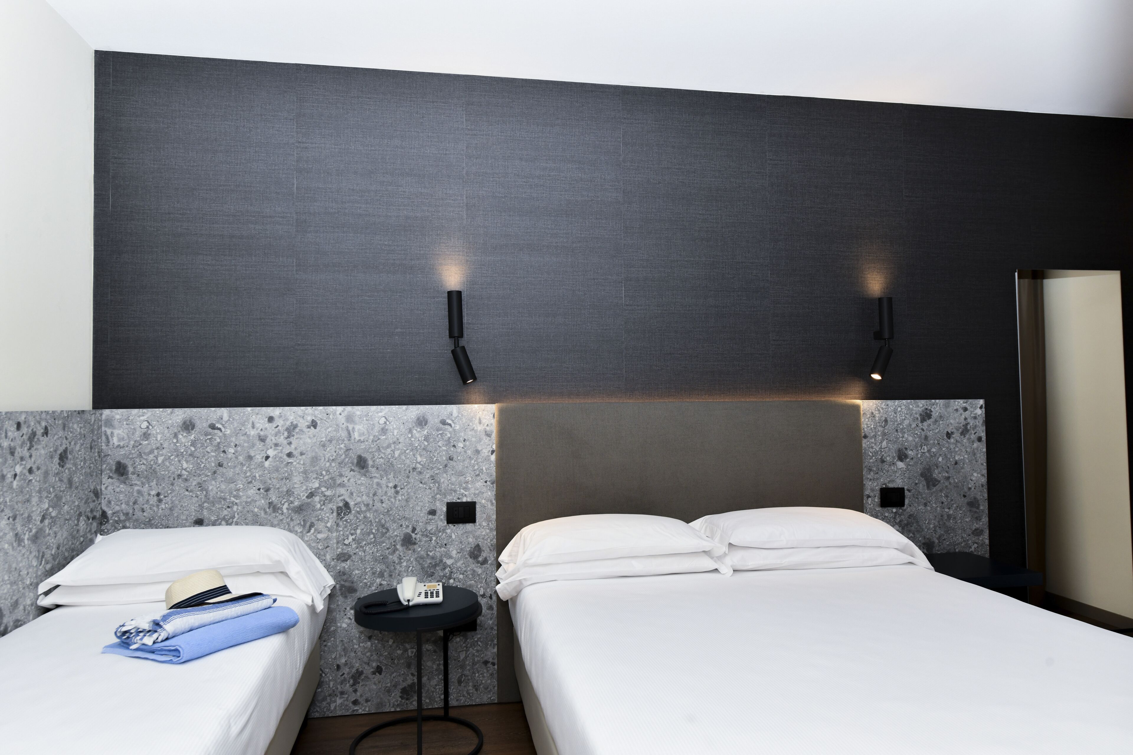 A hotel room with two beds, a small table, and a wall-mounted phone.
