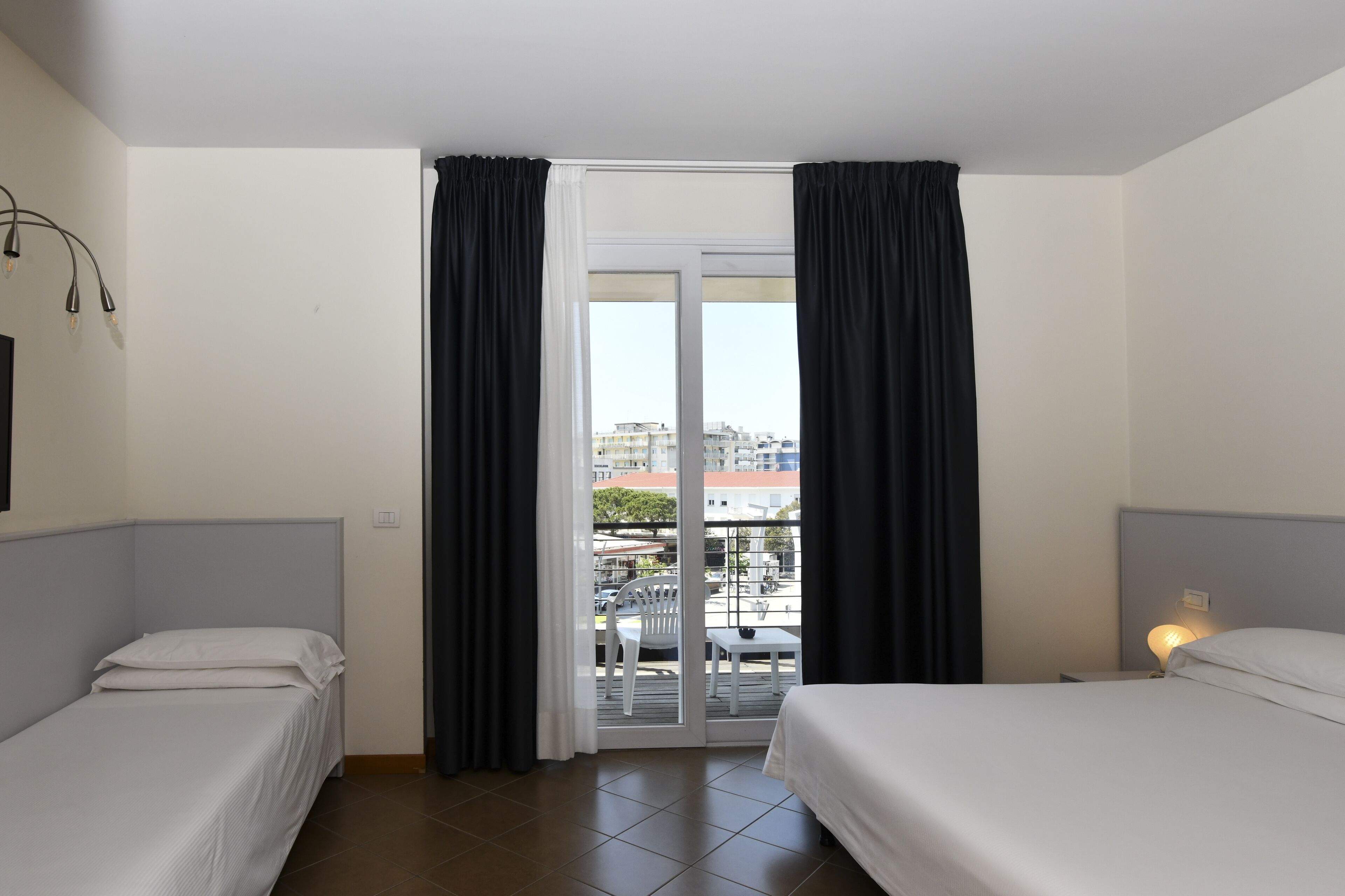 A hotel room with two beds, a balcony with a table and chairs, and a view of buildings outside.