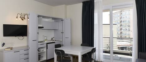 A compact living space with a kitchenette, a dining area, and a balcony with a city view.